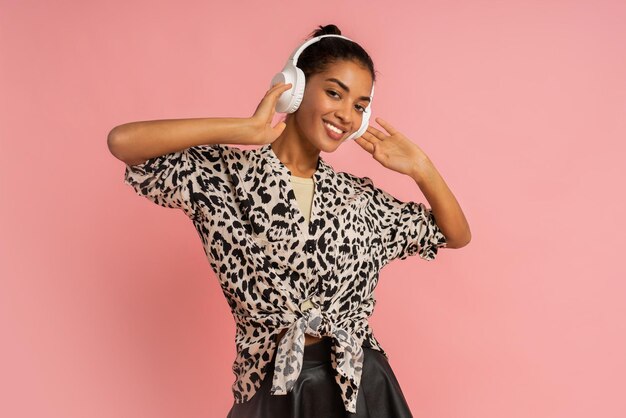 Smiling woman listenning music by earphones posing on pink background Wearing stylish blouse and leather skirt