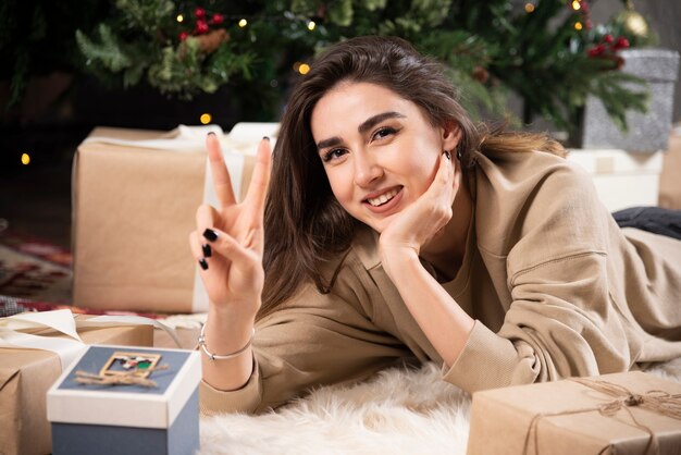 Smiling woman lying down on fluffy carpet with Christmas presents .