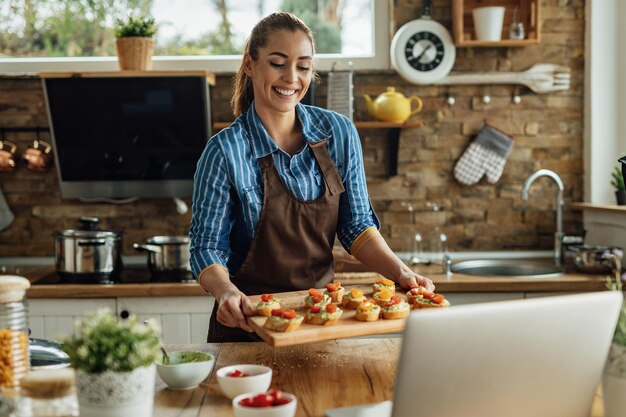 Smiling woman making a cooking blog and showing healthy bruschetta she has prepared in the kitchen