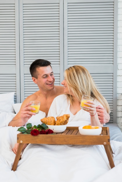 Smiling woman and man with glasses in bed near food on breakfast table