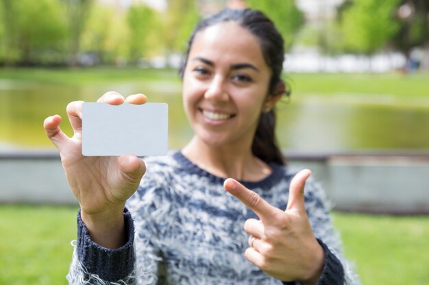 Smiling woman pointing at blank business card in city park