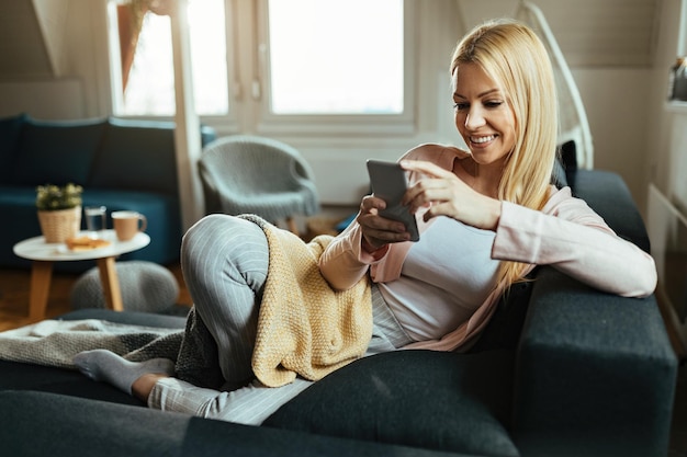 Smiling woman relaxing in her living room and text messaging on mobile phone.