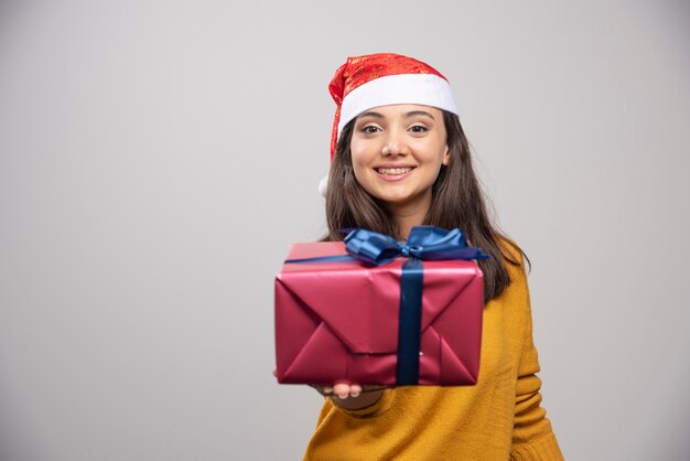 Smiling woman in Santa hat showing a gift box. 