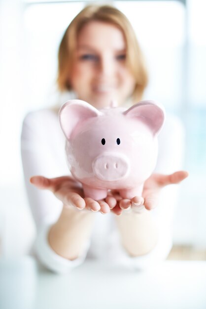 Smiling woman saves money in piggy bank