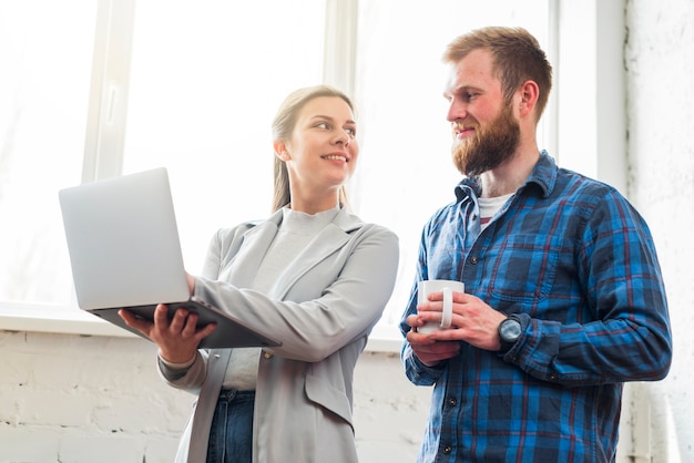 Free Photo smiling woman showing laptop to her colleague at workplace