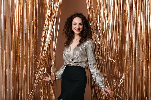 Smiling woman in silver outfit happily poses on gold background