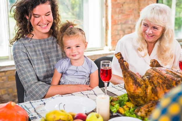 Smiling woman sitting with child at table near aged lady