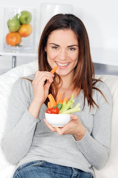 Smiling woman on sofa with vegetable salad