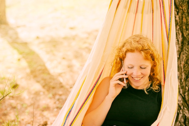 Free photo smiling woman speaking on phone in hammock