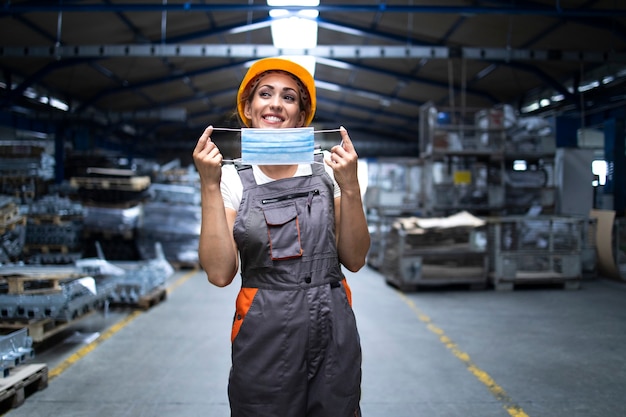 Free photo smiling woman in uniform and hardhat putting on hygienic mask as corona virus prevention