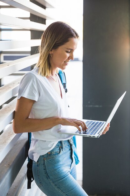 Smiling woman using laptop near wall