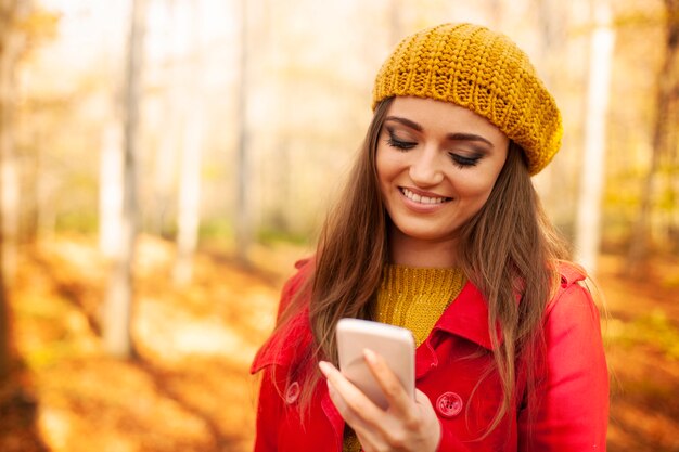 Smiling woman using mobile phone in park during the autumn