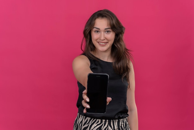 Smiling woman wearing black undershirt held out phone on pink wall