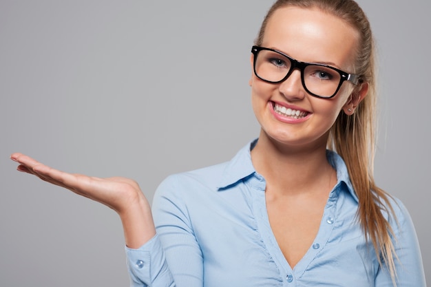 Smiling woman wearing fashion glasses presenting something on copy space