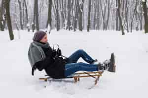 Free photo smiling woman wearing a warm clothes sitting on sledge over the snowy landscape