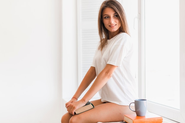 Smiling woman with book sitting on window sill