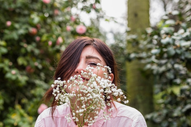 Smiling woman with bunch of plants near pink flowers growing on bushes