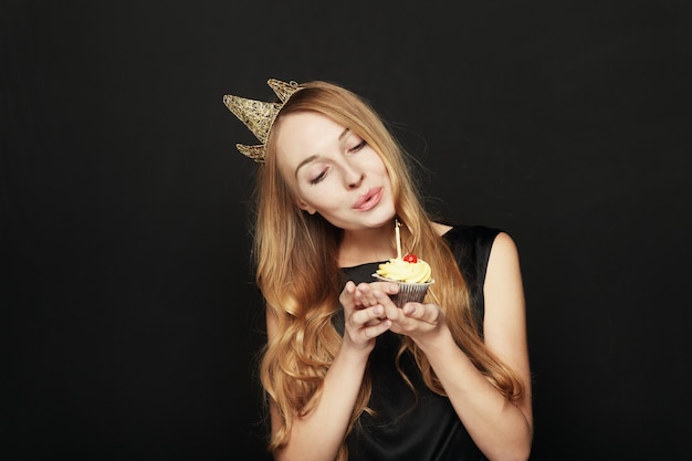 Smiling woman, with a crown, holding a birthday cupcake