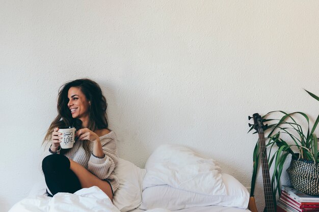 Smiling woman with cup on bed