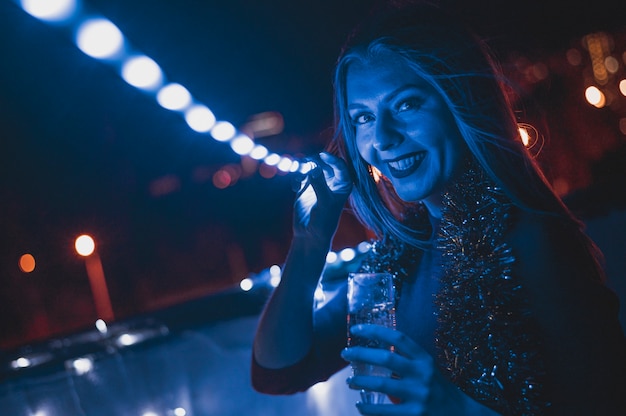 Free photo smiling woman with a glass of champagne and blue lamps