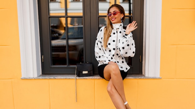 Free photo smiling woman with legs in stylish spring clothes with small bag posing on the street on yellow.