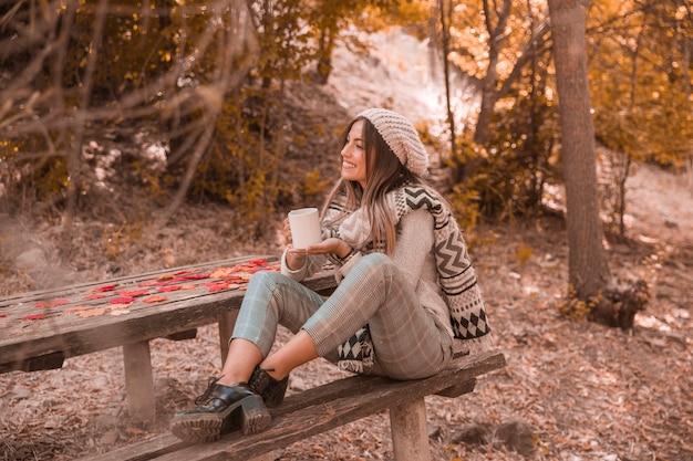 Free photo smiling woman with mug near table in park