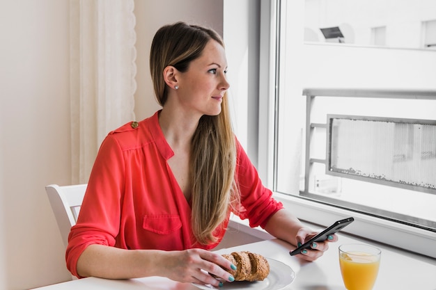 Free Photo smiling woman with smartphone looking out window