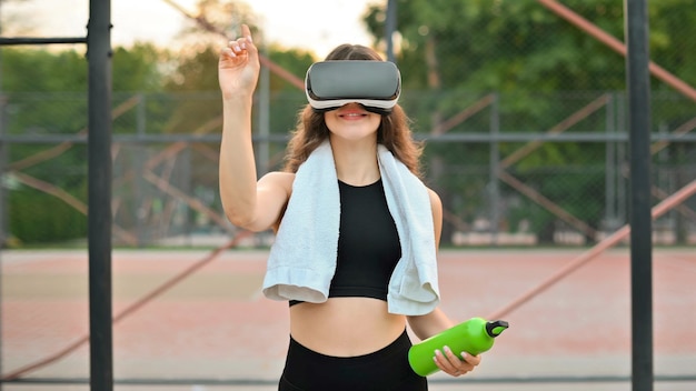 Free photo smiling woman with towel using vr headset in a tracksuit holding a water bottle on a sports field