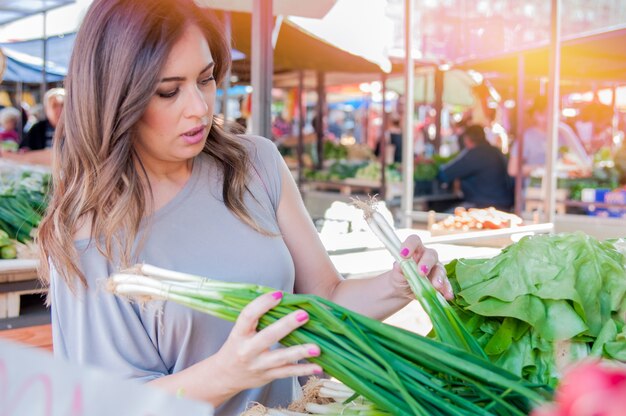 smiling woman with vegetable at market store. woman choosing fresh vegetables in green market. Portrait of beautiful young woman choosing green leafy vegetables