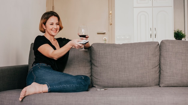 Smiling woman with wine and remote controller