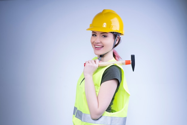 Smiling woman in a yellow helmet stands with a hammer on her shoulder