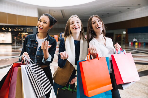 Smiling women with bags gesturing at camera