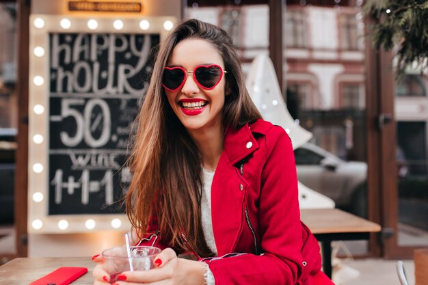 Smiling wonderful girl in stylish sunglasses spending weekend morning in outdoor cafe