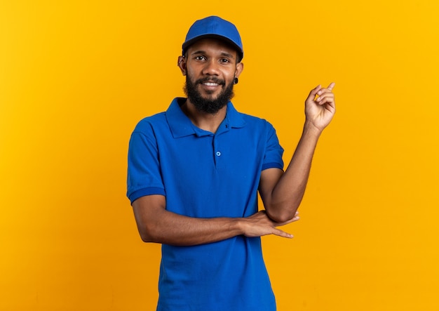 Smiling young afro-american delivery man pointing at side isolated on orange background with copy space