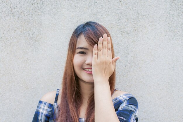 Smiling young beautiful asian woman closing her eyes with hands on concrete wall background. Vintage effect style pictures.Smiling young beautiful asian woman closing her eyes with hands on concrete wall background. Vintage effect style pictures.