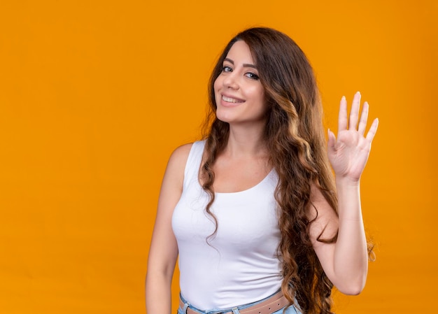 Smiling young beautiful girl gesturing hi on isolated orange space with copy space