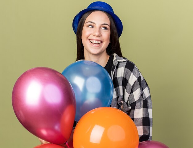 Smiling young beautiful girl wearing blue hat standing behind balloons 