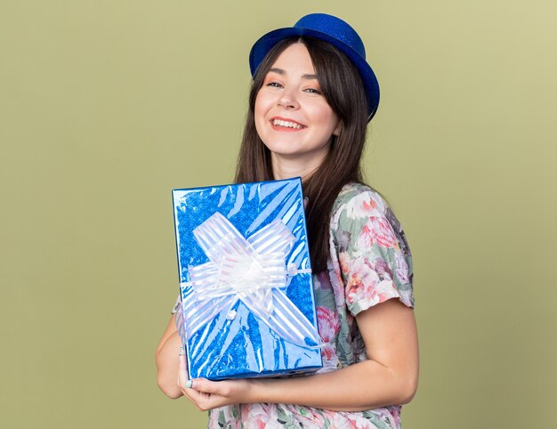 Smiling young beautiful girl wearing party hat holding gift box 