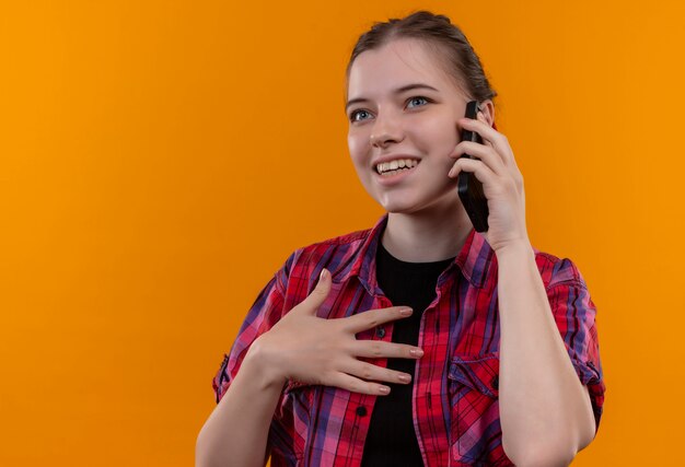 Smiling young beautiful girl wearing red shirt speaks on phone on isolated yellow background with copy space