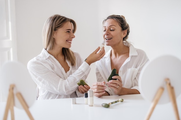 Free Photo smiling young blonde caucasian girls are trying out new cosmetic product while sitting at table in studio. beauty and personal care, skin and face care concept