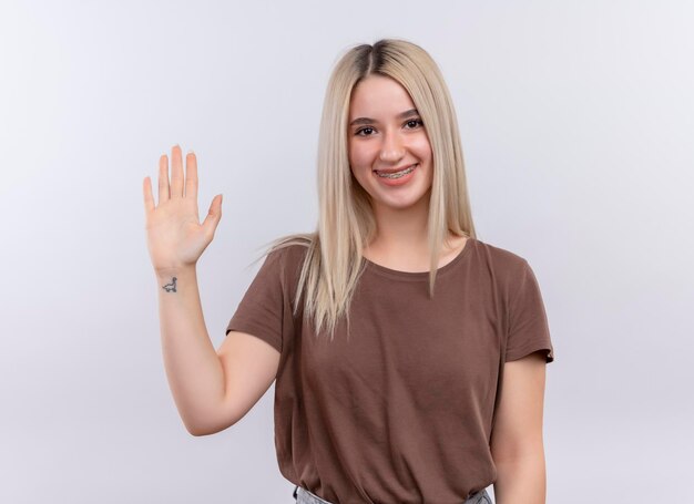 Smiling young blonde girl in dental braces gesturing hi on isolated white space