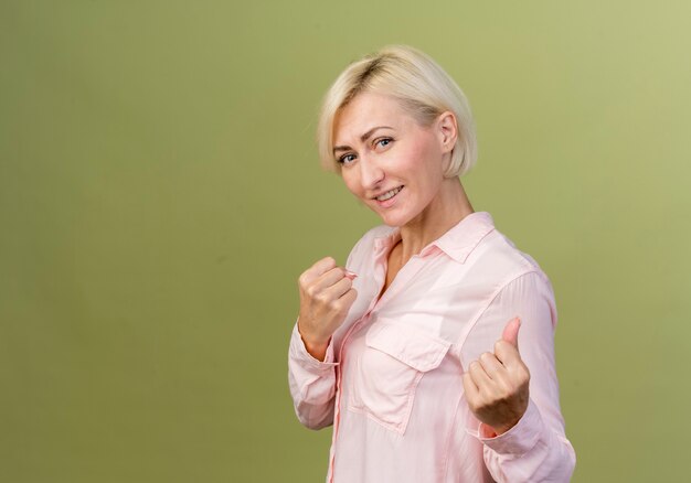 Smiling young blonde slavic woman standing in fighting pose isolated on olive green