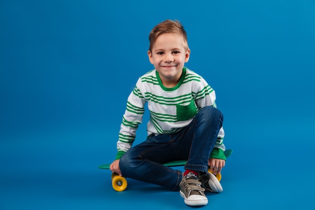 Smiling young boy sitting on skateboard and looking