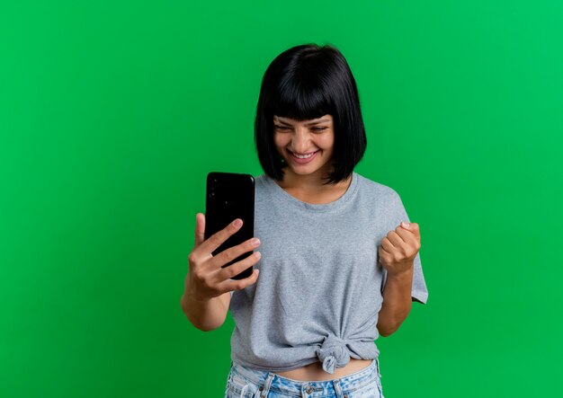 Smiling young brunette caucasian woman keeps fist looking at phone