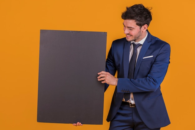 Free photo a smiling young businessman holding blank black placard against an orange backdrop