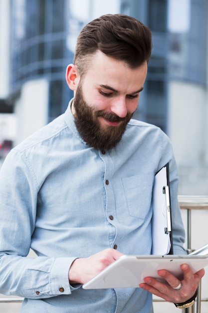 Free Photo smiling young businessman holding clipboard using digital tablet