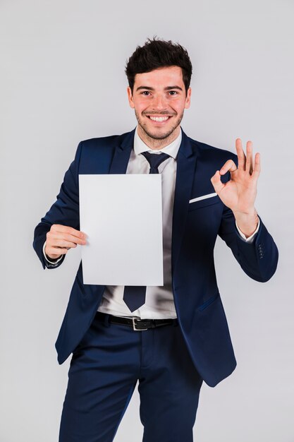 Smiling young businessman holding white paper in hand showing ok sign