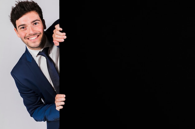 Smiling young businessman peeking from the black placard