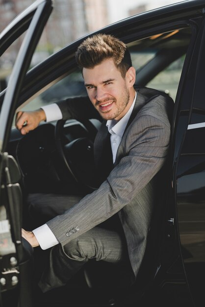 Smiling young businessman sitting in car with an open door