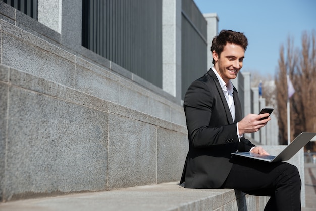 Smiling young businessman sitting outdoors chatting by phone.